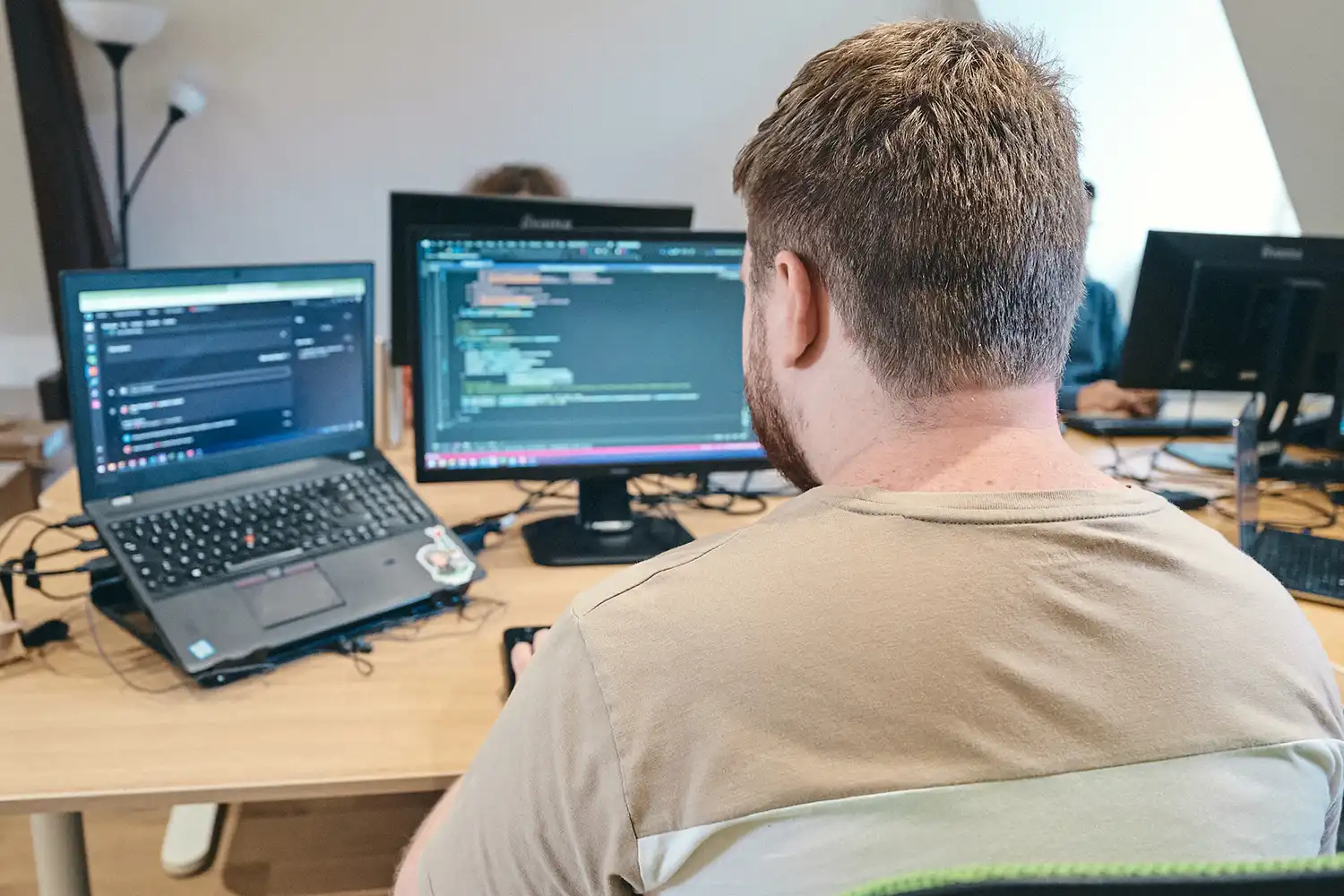 ONIRYX-Equipe-1 Un homme de dos travaille sur un ordinateur avec deux écrans affichant du code, dans un bureau moderne.