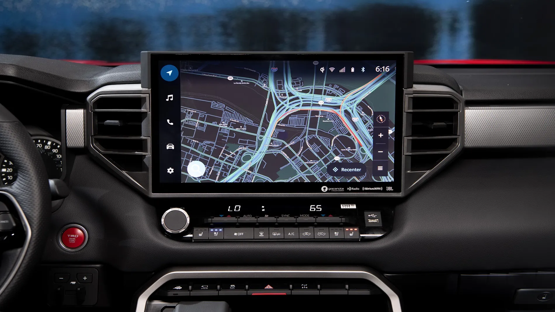 Écran de navigation d'une Toyota affichant une carte routière détaillée, intégré dans un tableau de bord noir avec commandes de climatisation.